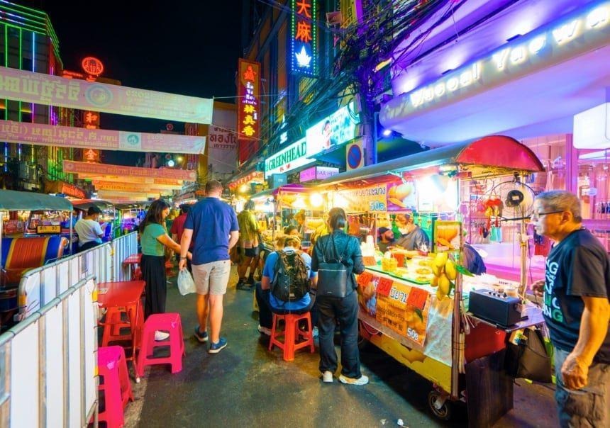 Bright food stalls, neon signs, diners, and pedestrians along Yaowarat Road at night